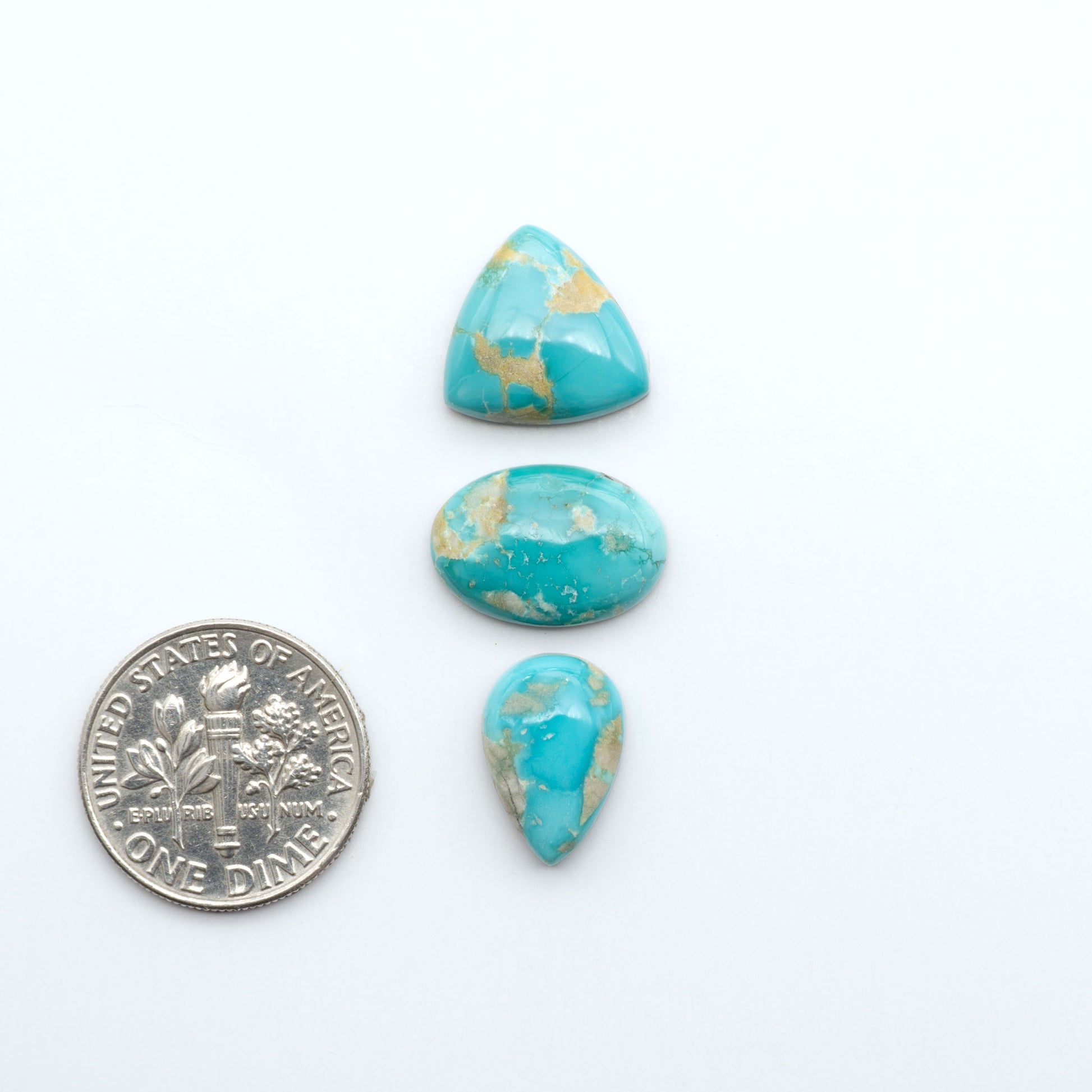 Fox Turquoise cabochons, polished gemstones with natural matrix on a white background, with a US dime for scale