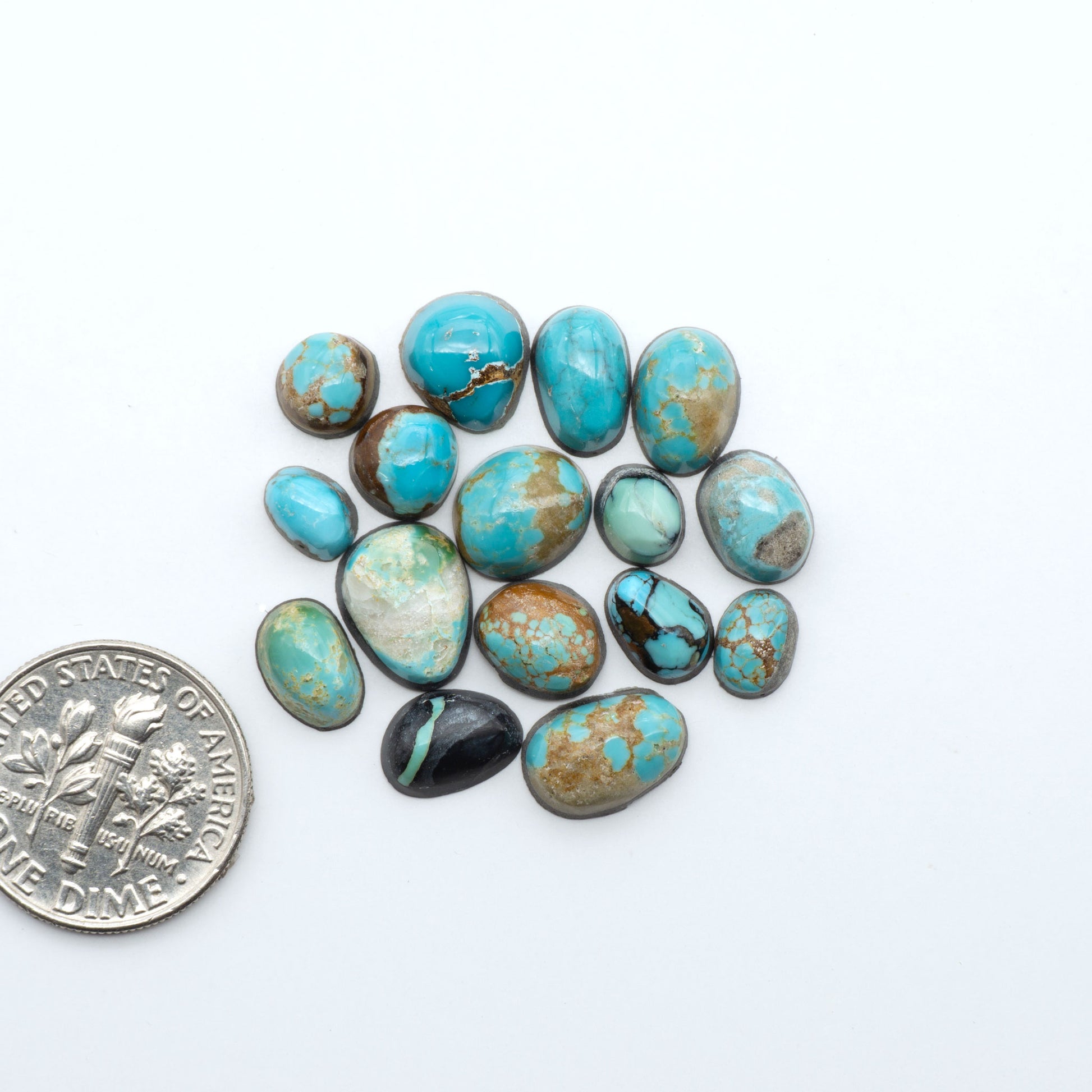 Assorted turquoise cabochon gemstones with varied colors and matrix on a white background with a US dime for scale