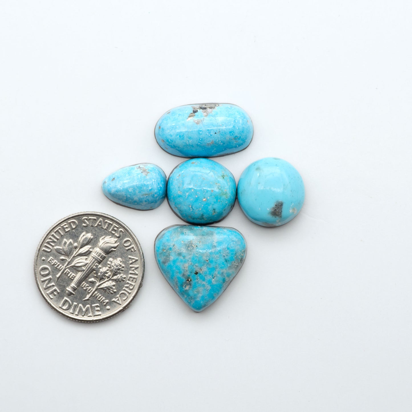 Nacozari Turquoise cabochons, blue to greenish-blue gemstones with black or brown matrix and pyrite on a white background with a US dime for scale