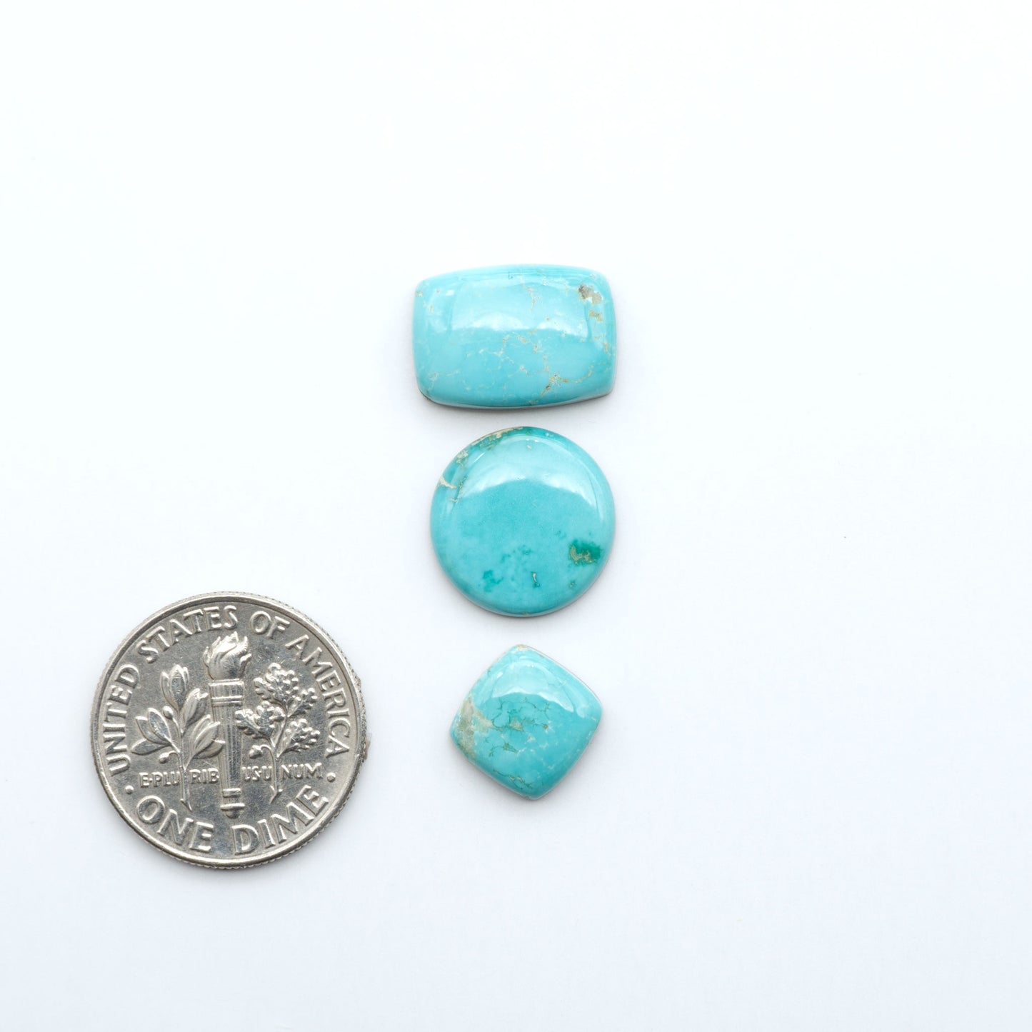 Fox Turquoise cabochons, polished gemstones with natural matrix on a white background, with a US dime for scale