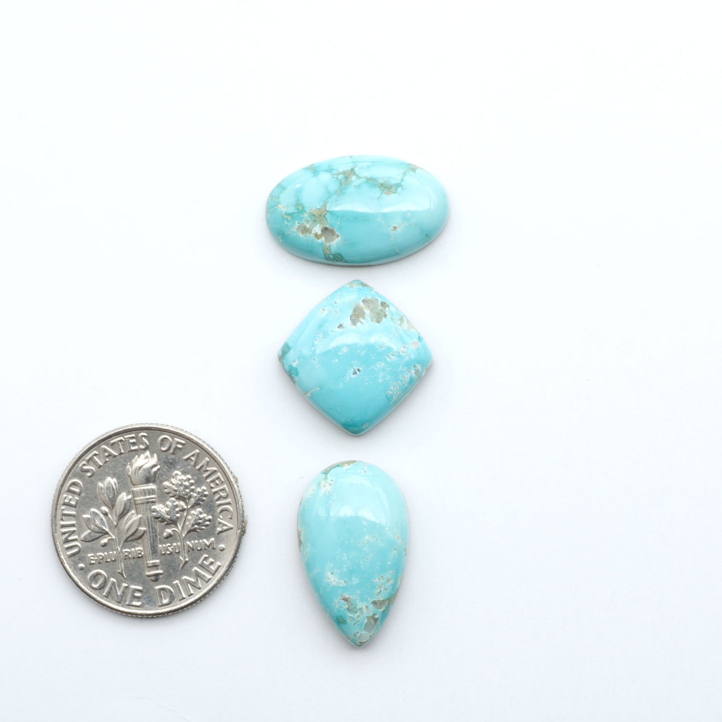 Fox Turquoise cabochons, polished gemstones with natural matrix on a white background, with a US dime for scale