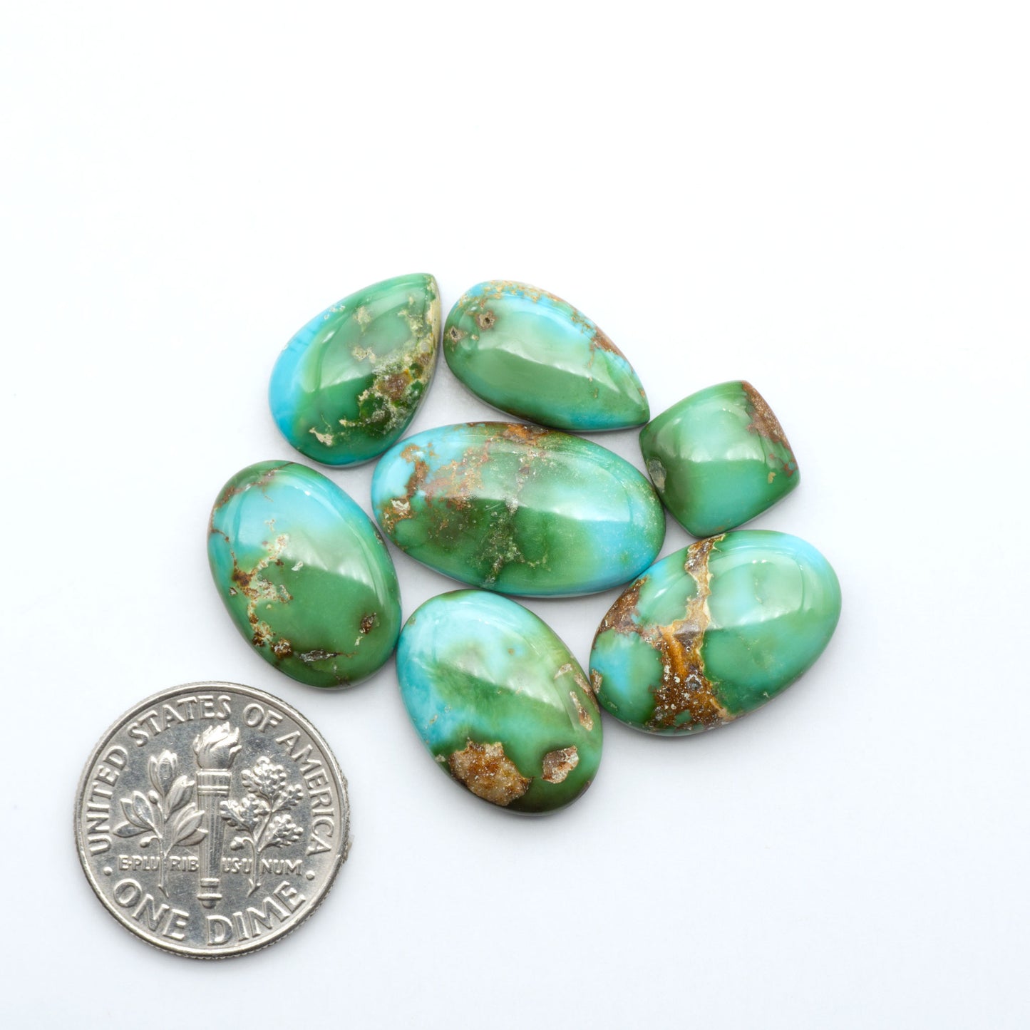 Sonoran Mountain Turquoise cabochons, blue-green color with natural matrix, polished stones on a white background, with a US dime for scale