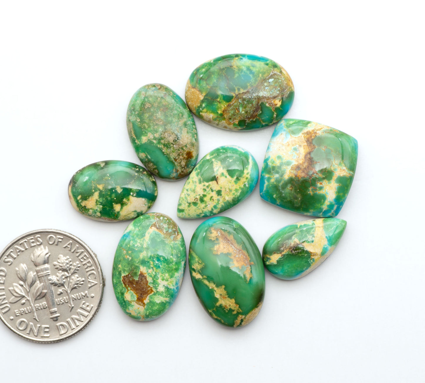 Sonoran Mountain Turquoise cabochons, blue-green color with natural matrix, polished stones on a white background, with a US dime for scale