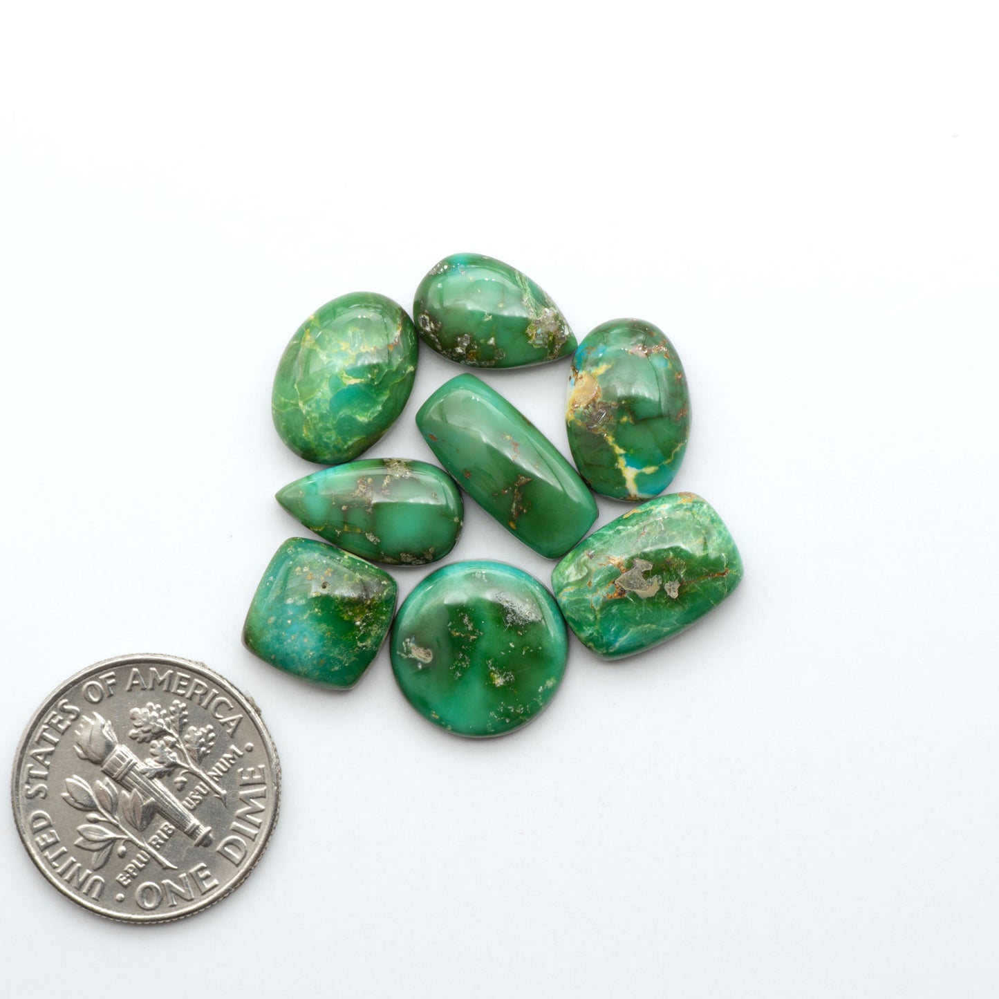 Sonoran Mountain Turquoise cabochons, blue-green color with natural matrix, polished stones on a white background, with a US dime for scale