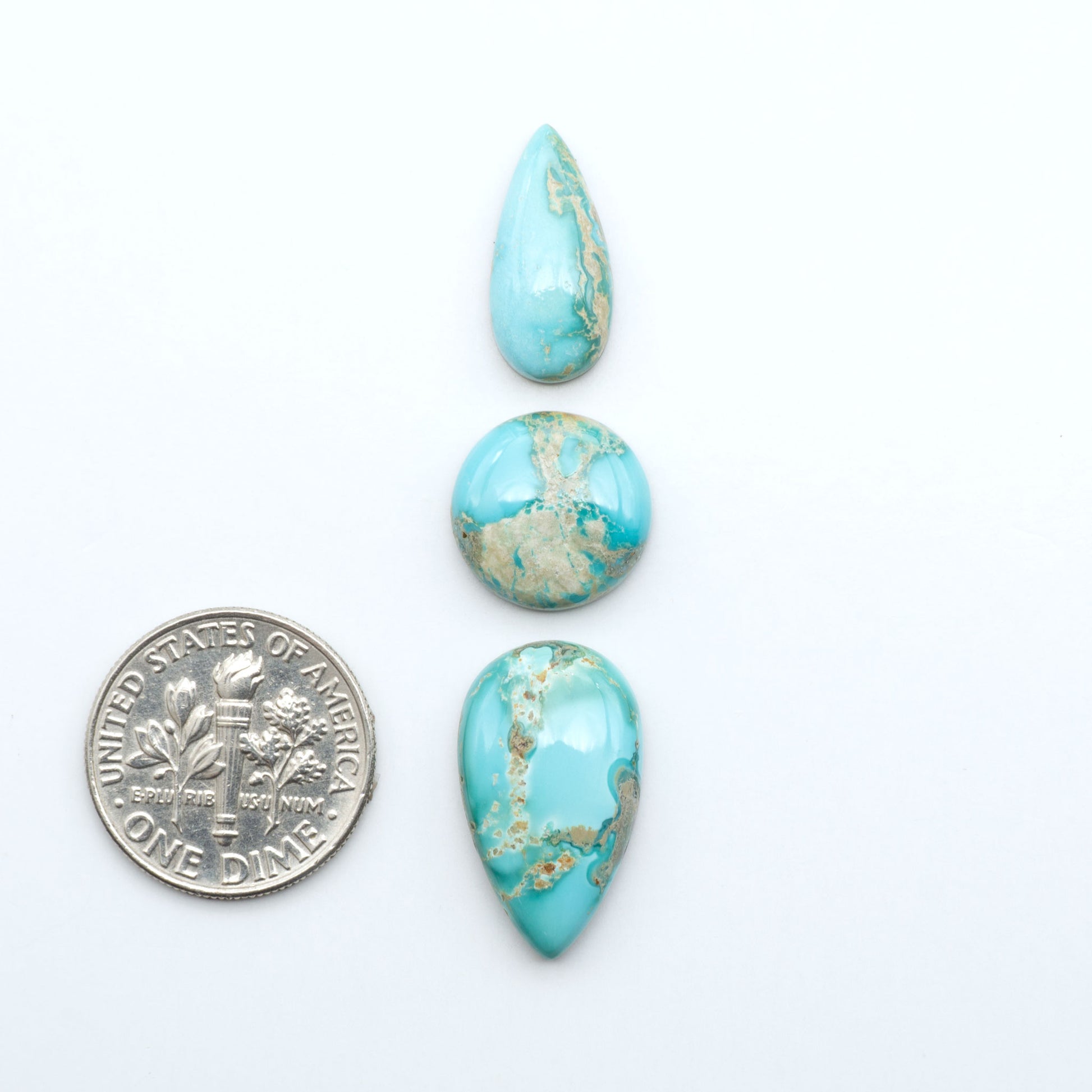 Fox Turquoise cabochons, polished gemstones with natural matrix on a white background, with a US dime for scale