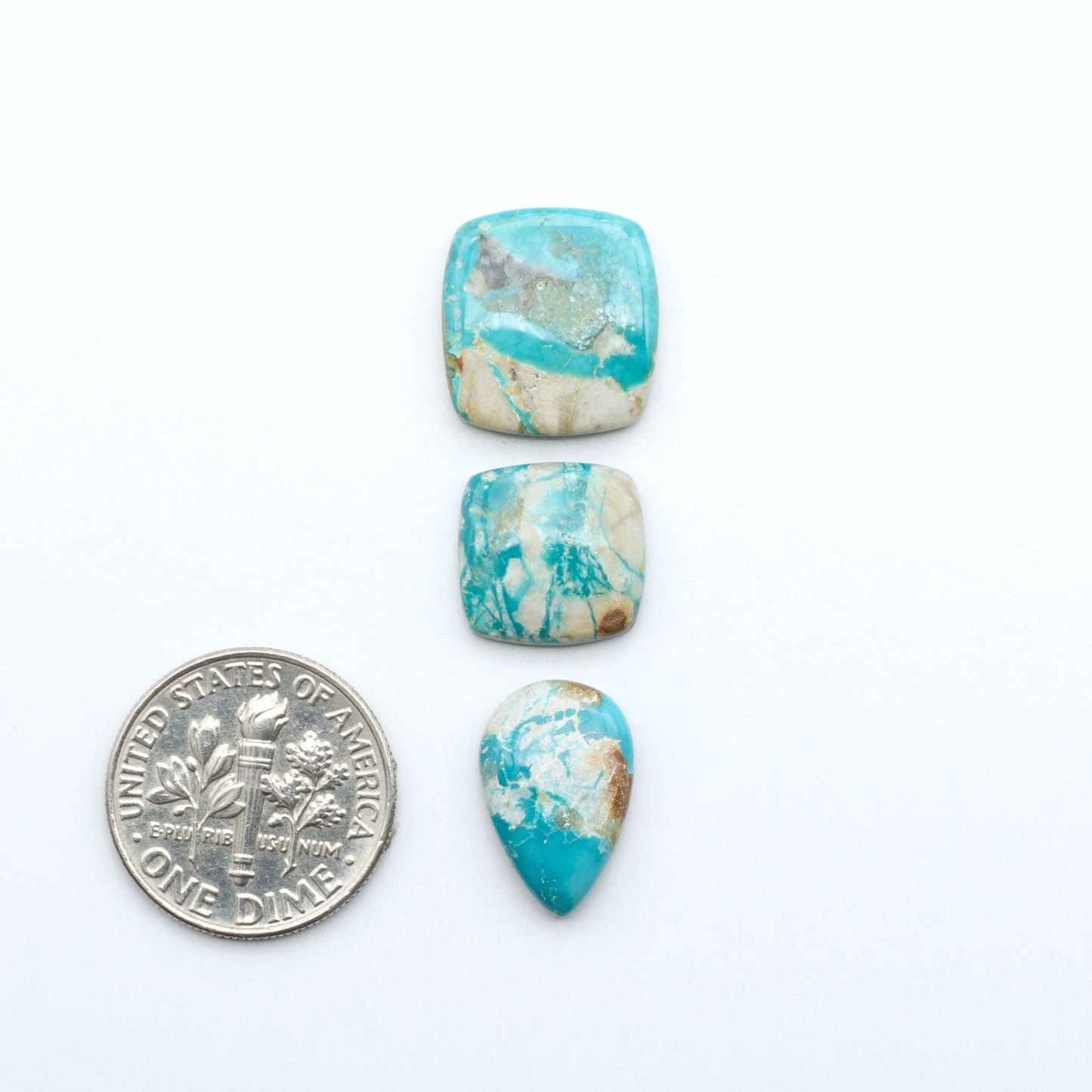 Fox Turquoise cabochons, polished gemstones with natural matrix on a white background, with a US dime for scale
