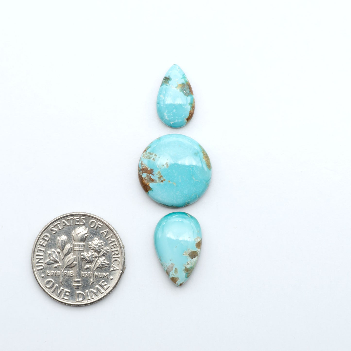 Fox Turquoise cabochons, polished gemstones with natural matrix on a white background, with a US dime for scale