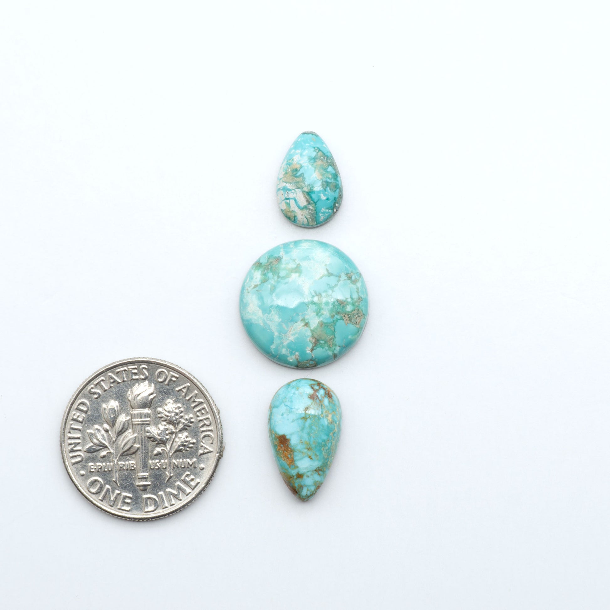 Fox Turquoise cabochons, polished gemstones with natural matrix on a white background, with a US dime for scale
