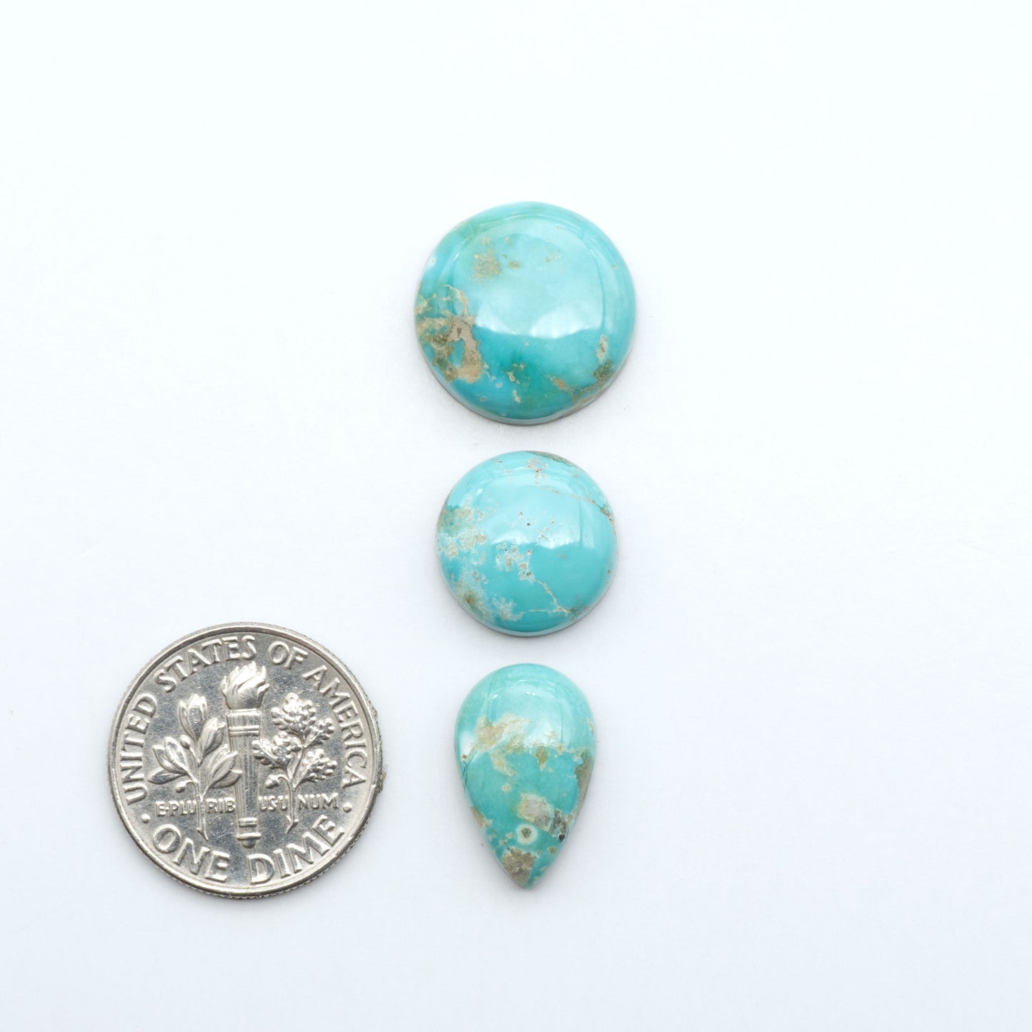 Fox Turquoise cabochons, polished gemstones with natural matrix on a white background, with a US dime for scale