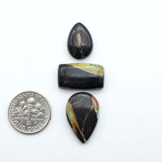 Black Jack turquoise cabochons, blue-green color with black matrix, polished stones on a white background with a US dime for scale