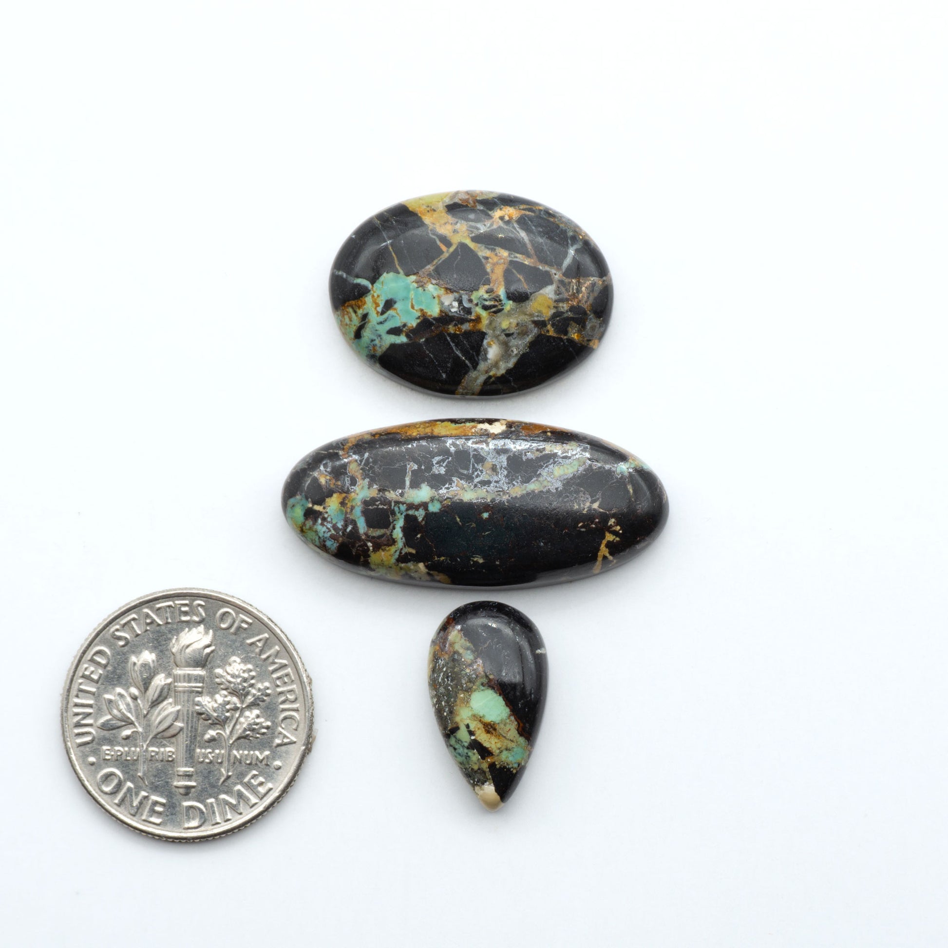 Black Jack turquoise cabochons, blue-green color with black matrix, polished stones on a white background with a US dime for scale