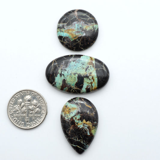 Black Jack turquoise cabochons, blue-green color with black matrix, polished stones on a white background with a US dime for scale