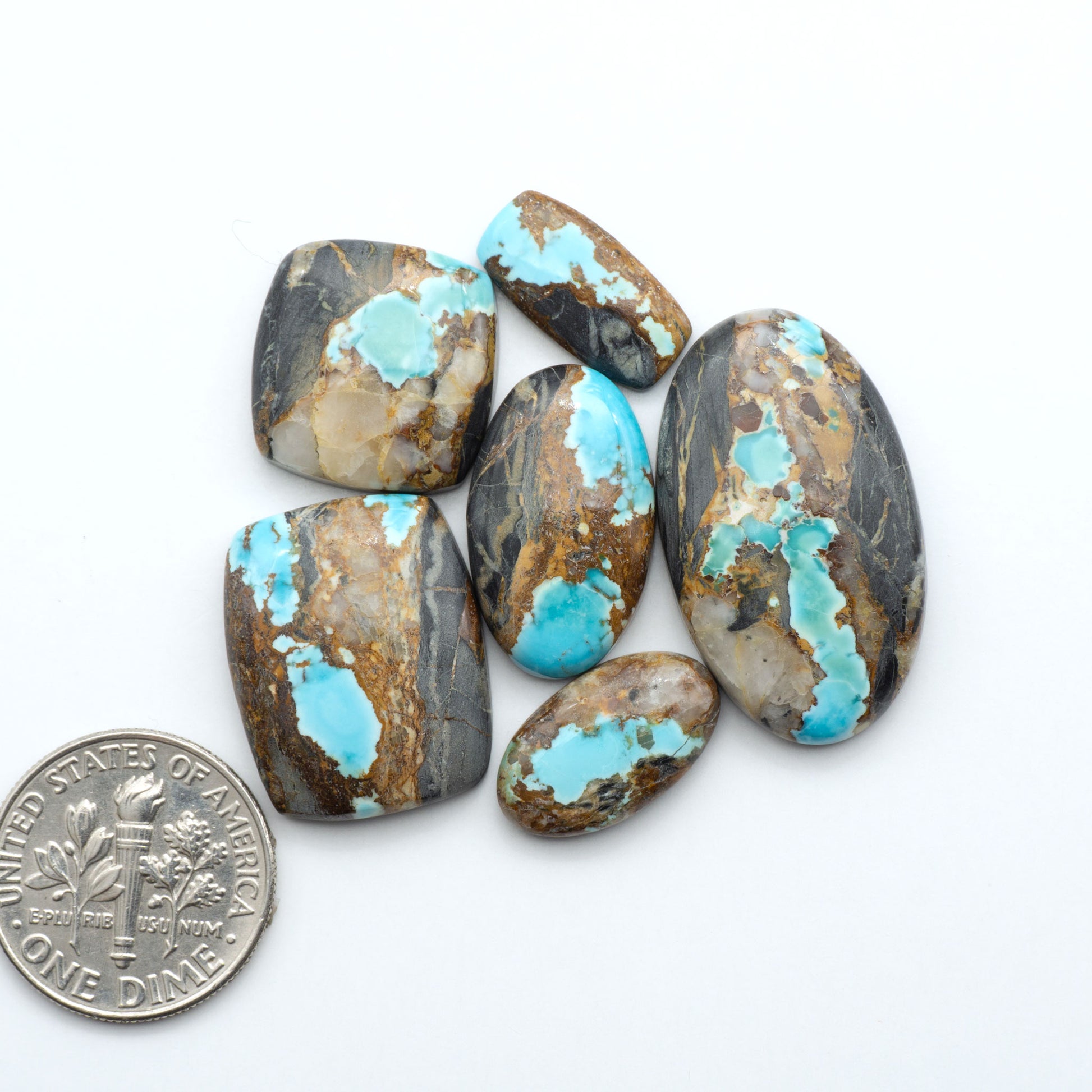Black Jack turquoise cabochons, blue-green color with black matrix, polished stones on a white background with a US dime for scale