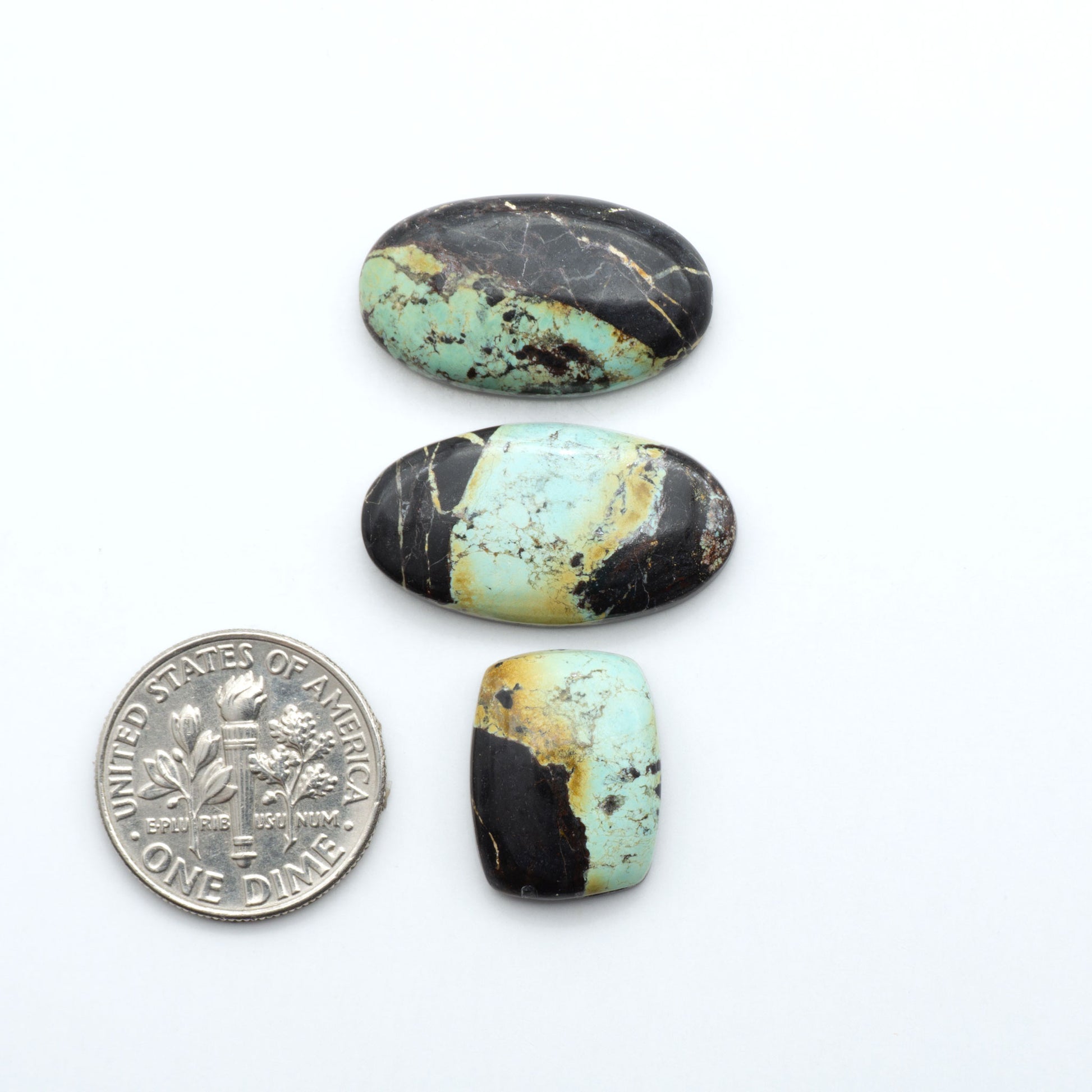 Black Jack turquoise cabochons, blue-green color with black matrix, polished stones on a white background with a US dime for scale