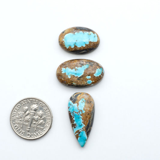 Black Jack turquoise cabochons, blue-green color with black matrix, polished stones on a white background with a US dime for scale