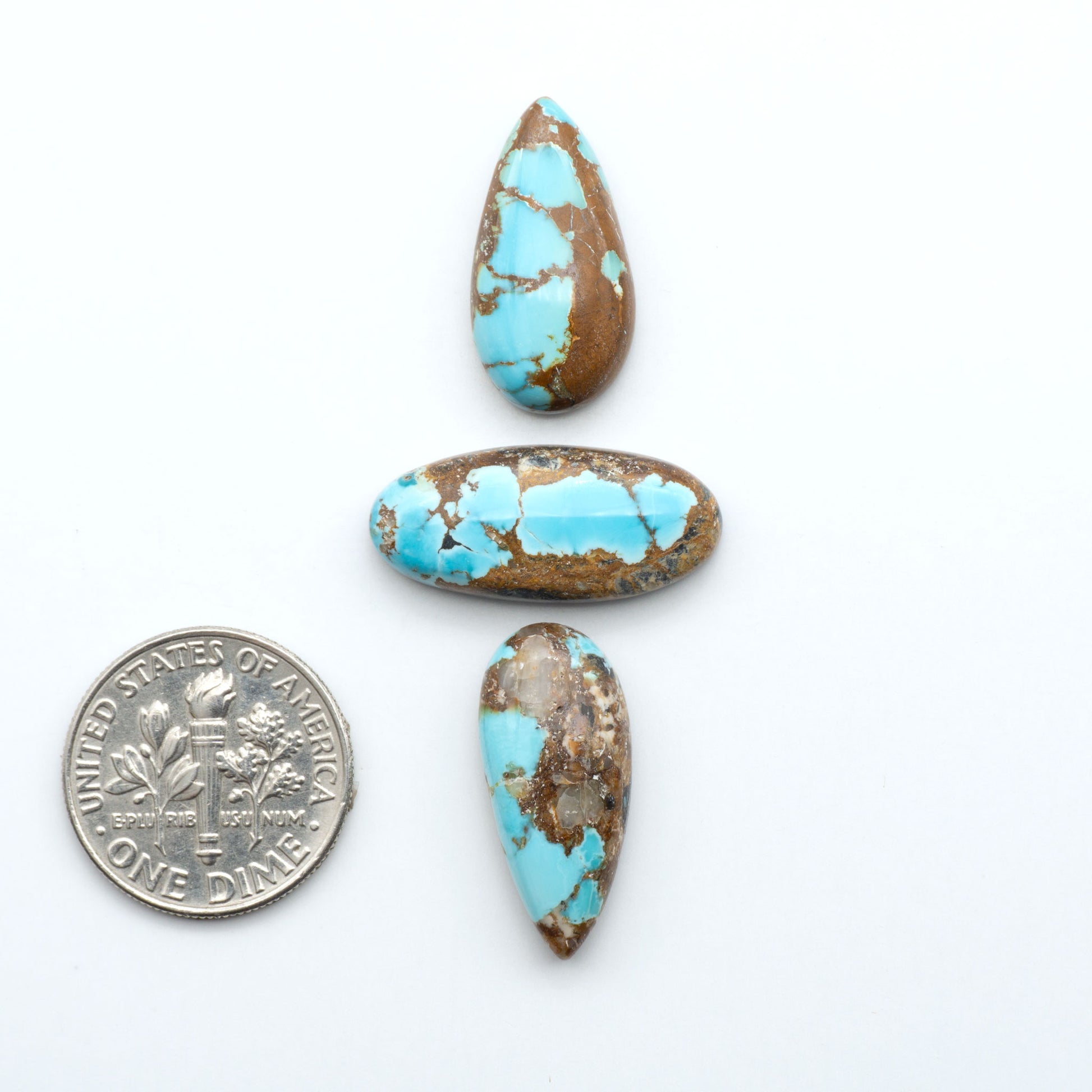 Black Jack turquoise cabochons, blue-green color with black matrix, polished stones on a white background with a US dime for scale