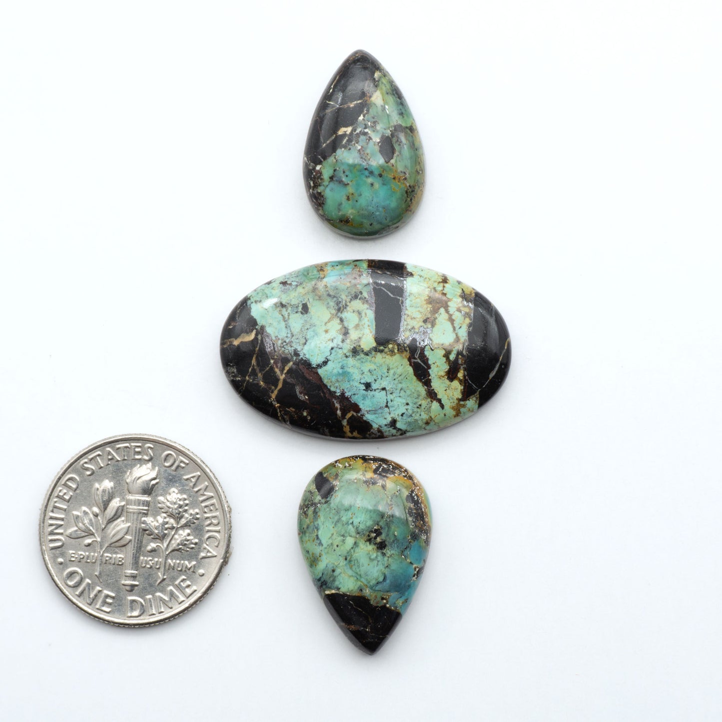 Black Jack turquoise cabochons, blue-green color with black matrix, polished stones on a white background with a US dime for scale