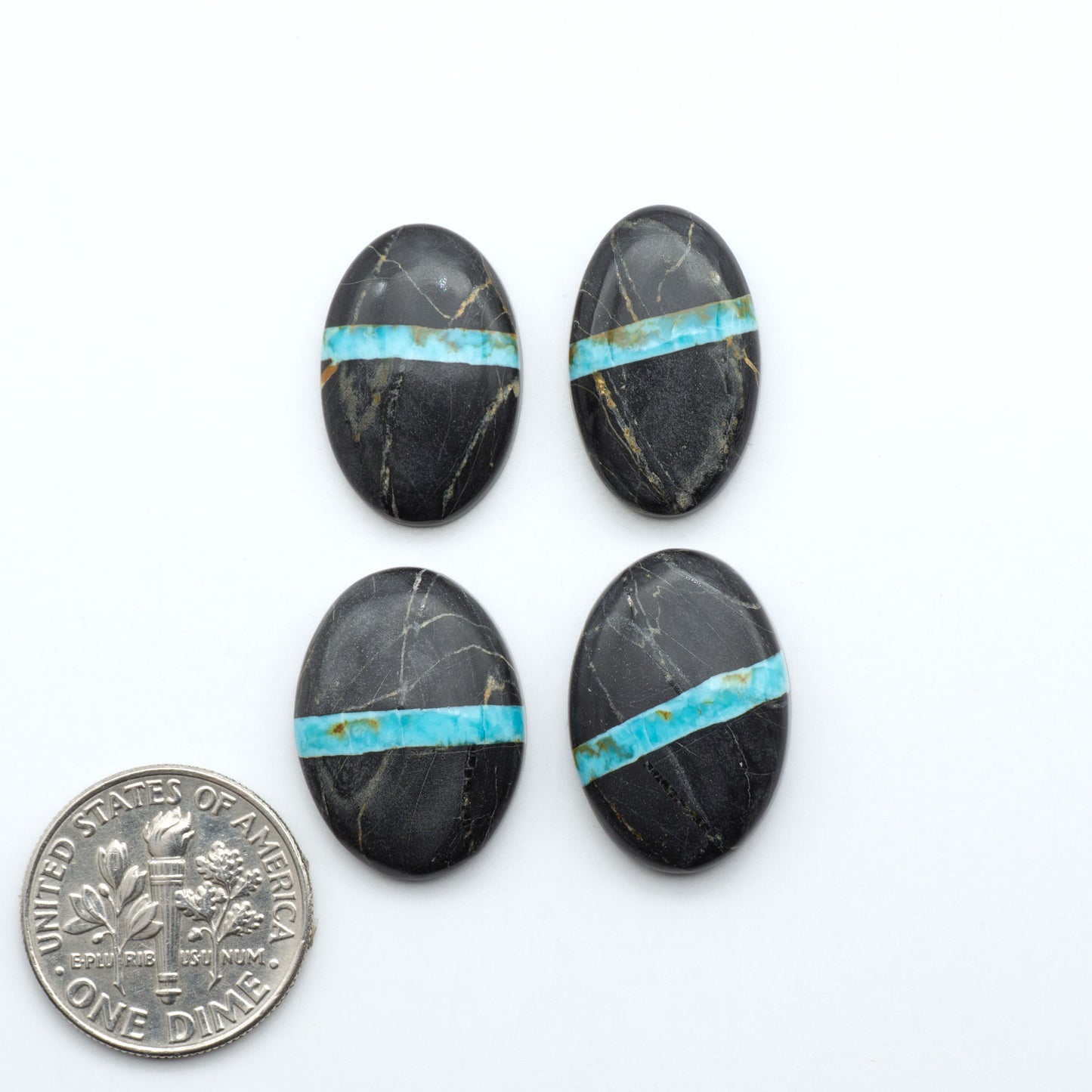 Black Jack turquoise cabochons, blue-green color with black matrix, polished stones on a white background with a US dime for scale