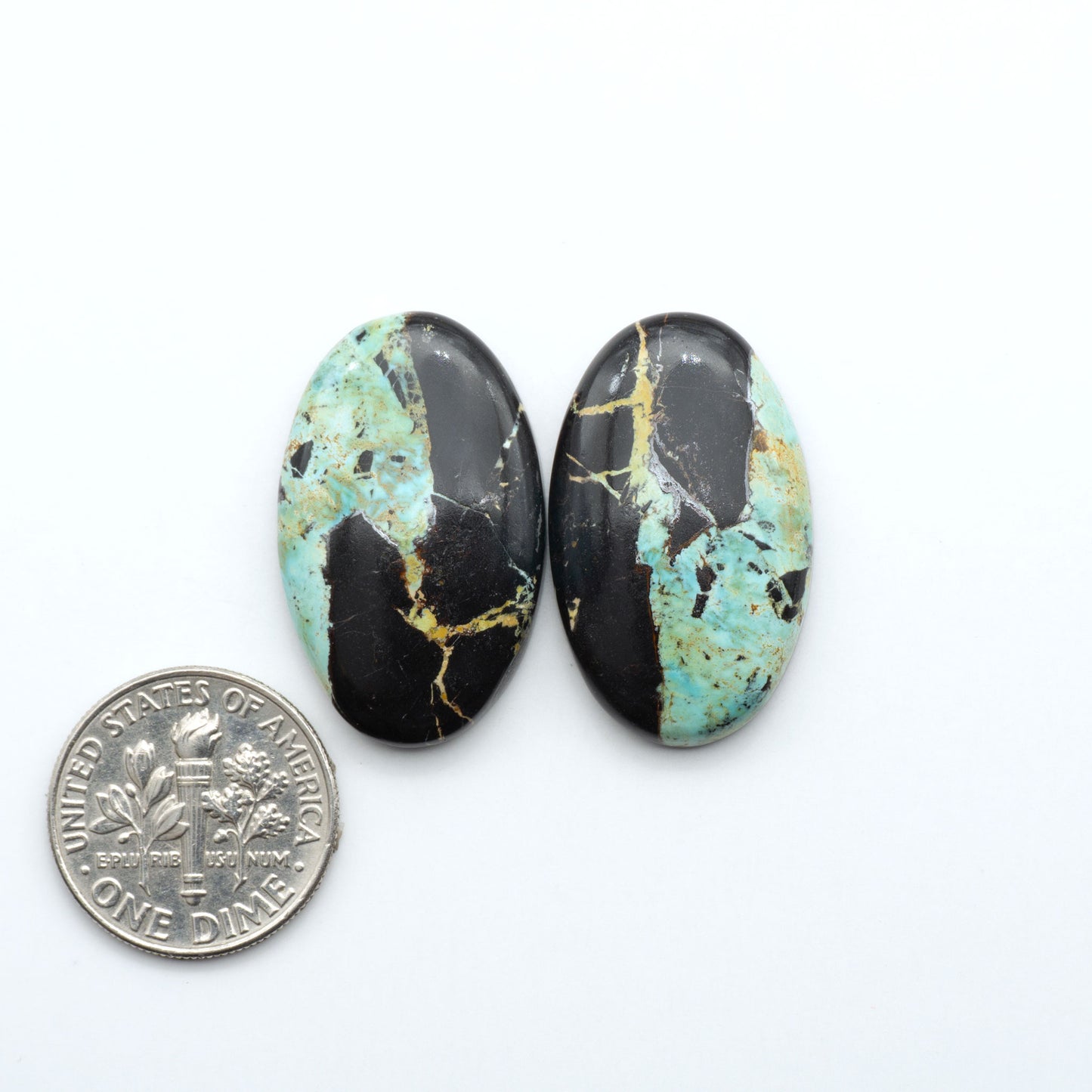 Black Jack turquoise cabochons, blue-green color with black matrix, polished stones on a white background with a US dime for scale