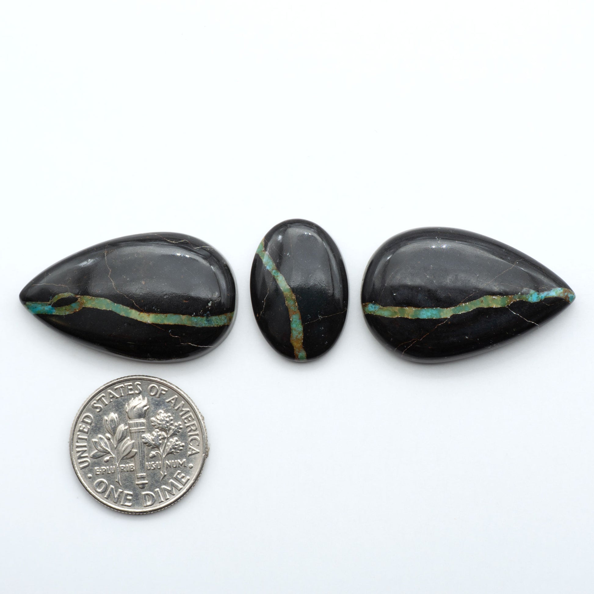 Black Jack turquoise cabochons, blue-green color with black matrix, polished stones on a white background with a US dime for scale
