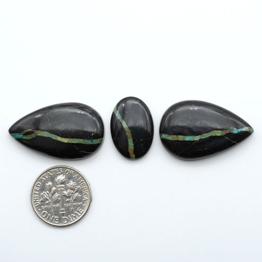 Black Jack turquoise cabochons, blue-green color with black matrix, polished stones on a white background with a US dime for scale