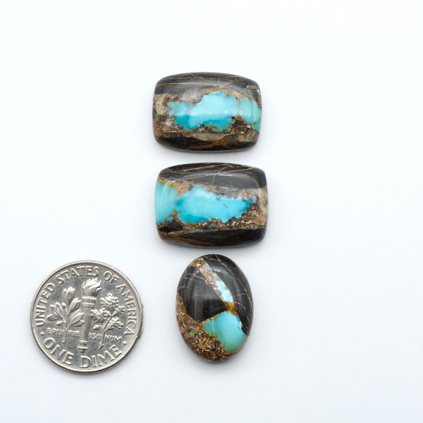 Black Jack turquoise cabochons, blue-green color with black matrix, polished stones on a white background with a US dime for scale