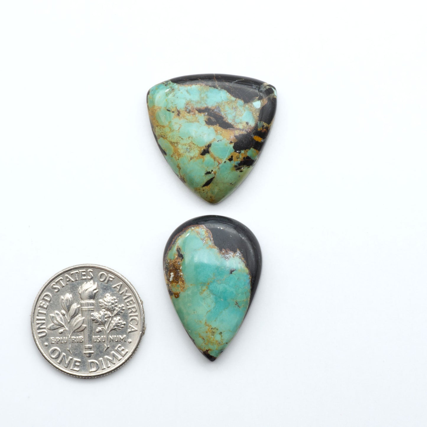 Black Jack turquoise cabochons, blue-green color with black matrix, polished stones on a white background with a US dime for scale