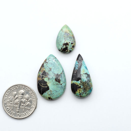 Black Jack turquoise cabochons, blue-green color with black matrix, polished stones on a white background with a US dime for scale
