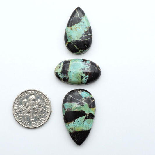 Black Jack turquoise cabochons, blue-green color with black matrix, polished stones on a white background with a US dime for scale