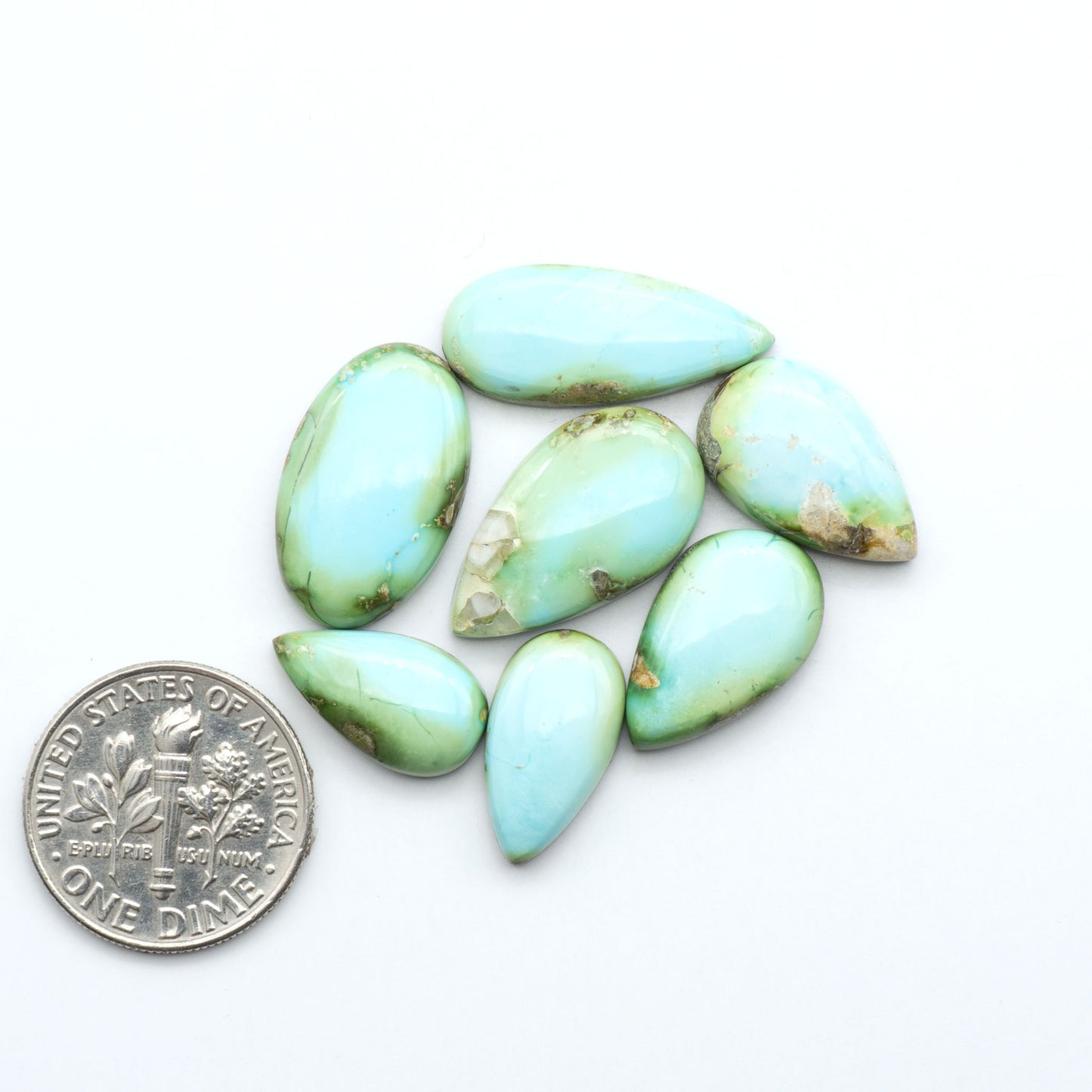 Sonoran Mountain Turquoise cabochons, blue-green color with natural matrix, polished stones on a white background, with a US dime for scale