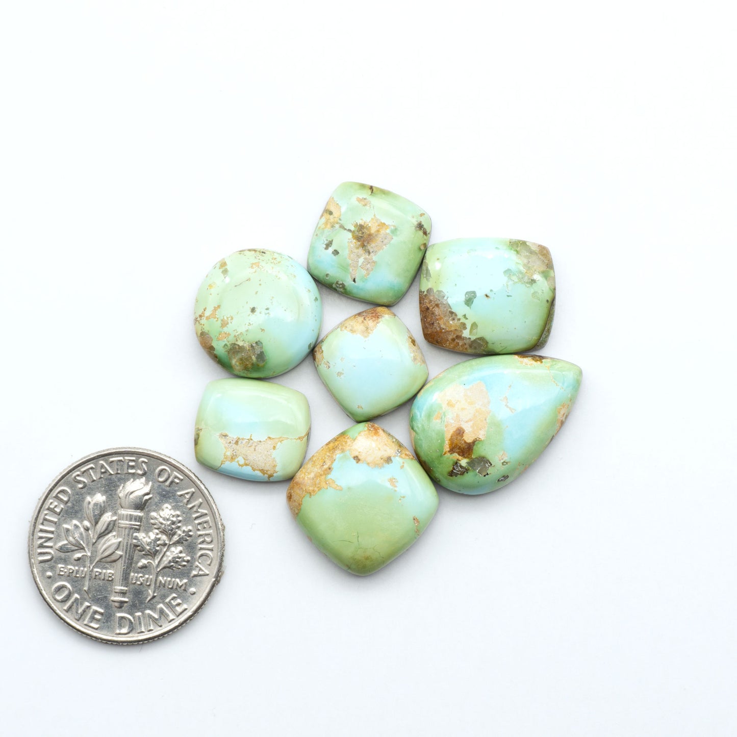 Sonoran Mountain Turquoise cabochons, blue-green color with natural matrix, polished stones on a white background, with a US dime for scale