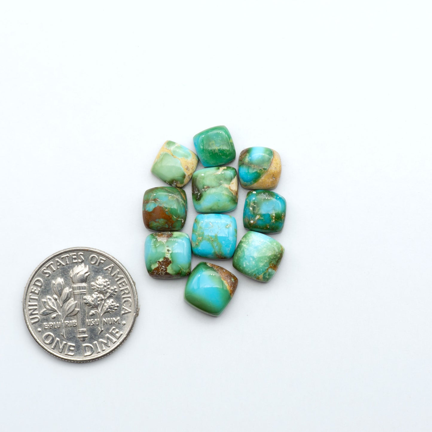 Sonoran Mountain Turquoise cabochons, blue-green color with natural matrix, polished stones on a white background, with a US dime for scale
