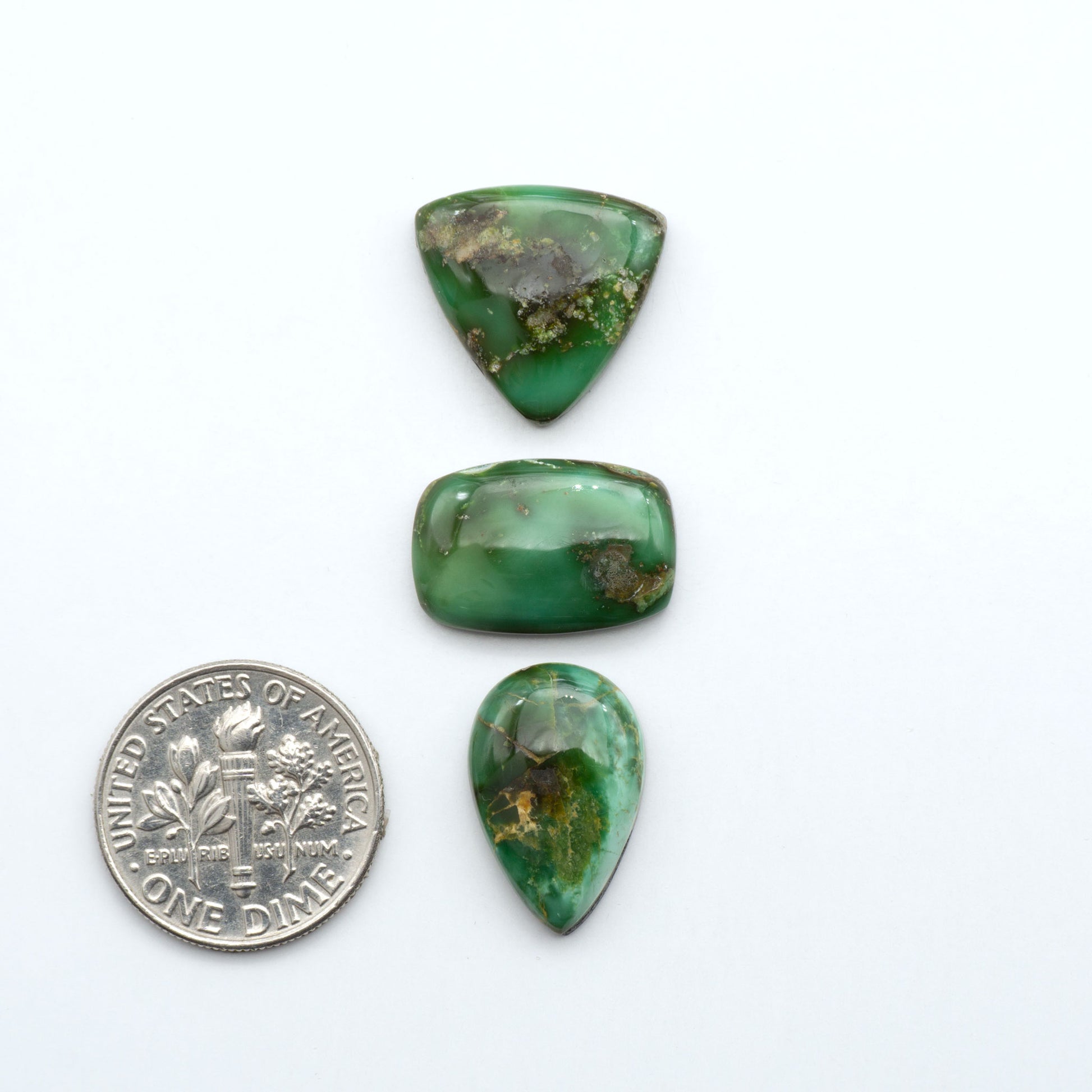 Sonoran Mountain Turquoise cabochons, blue-green color with natural matrix, polished stones on a white background, with a US dime for scale