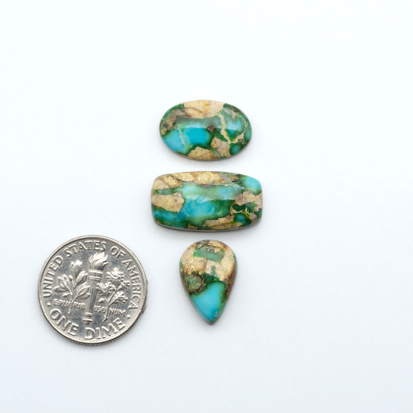 Sonoran Mountain Turquoise cabochons, blue-green color with natural matrix, polished stones on a white background, with a US dime for scale