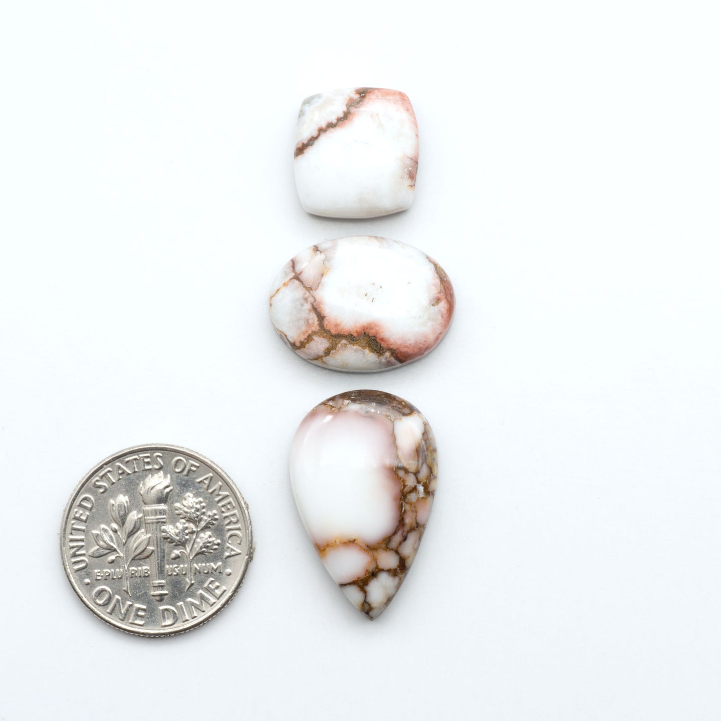 Wild Horse Magnesite cabochons, white gemstones with brown matrix on a white background, with a US dime for scale