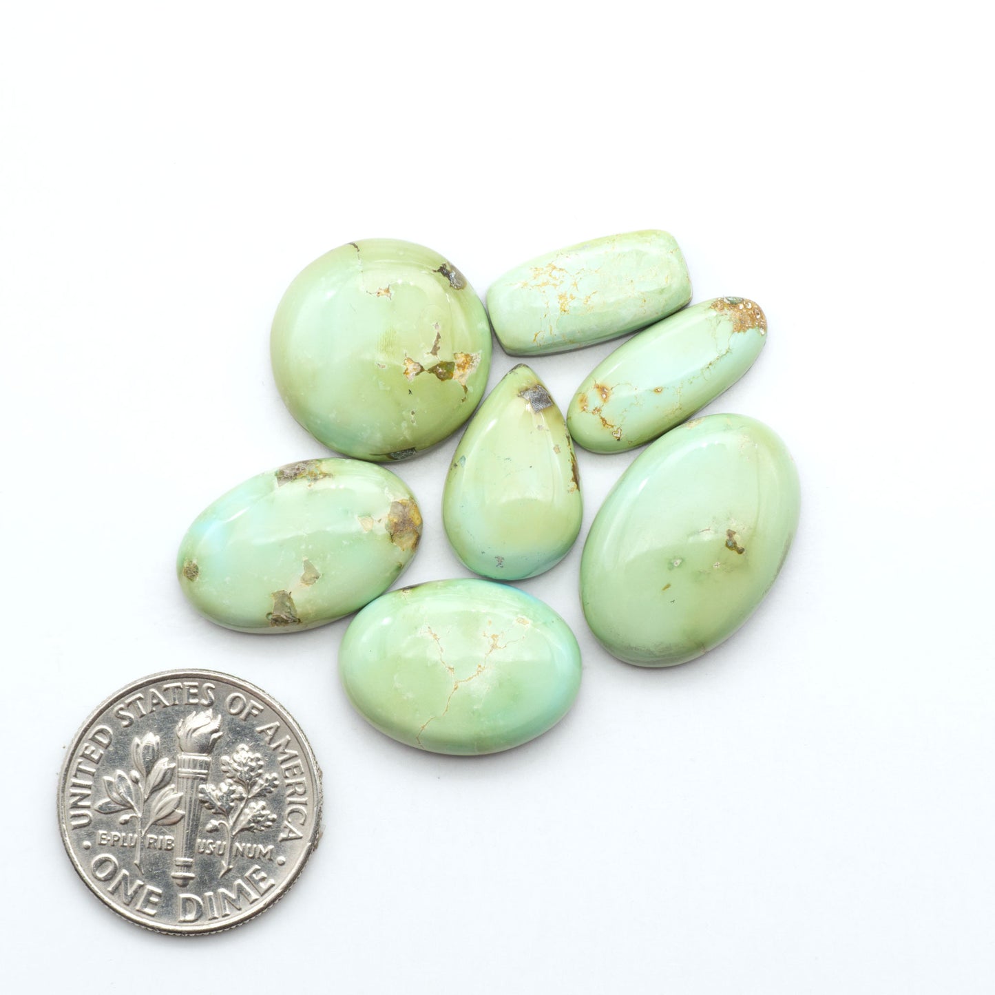 Sonoran Mountain Turquoise cabochons, blue-green color with natural matrix, polished stones on a white background, with a US dime for scale