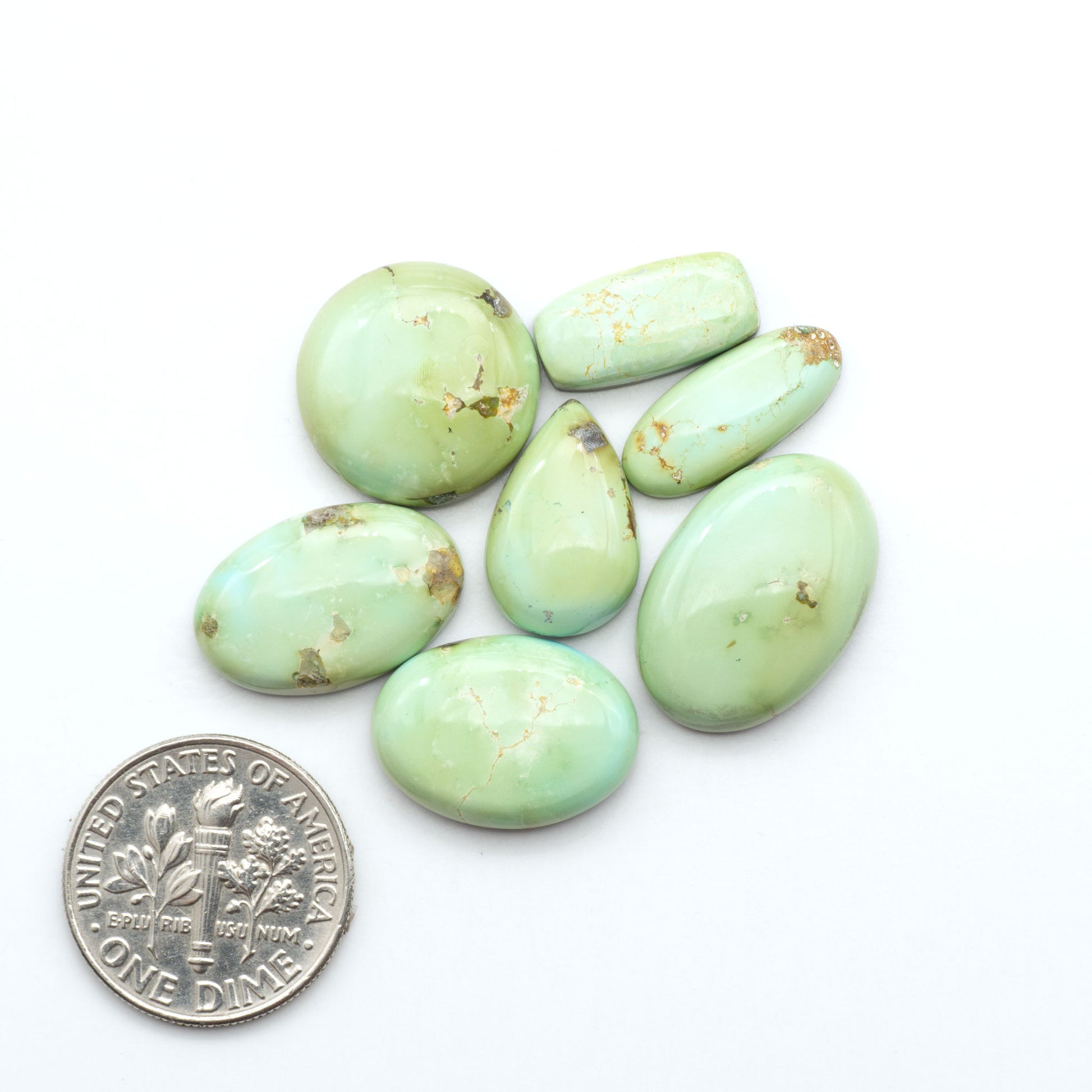 Sonoran Mountain Turquoise cabochons, blue-green color with natural matrix, polished stones on a white background, with a US dime for scale