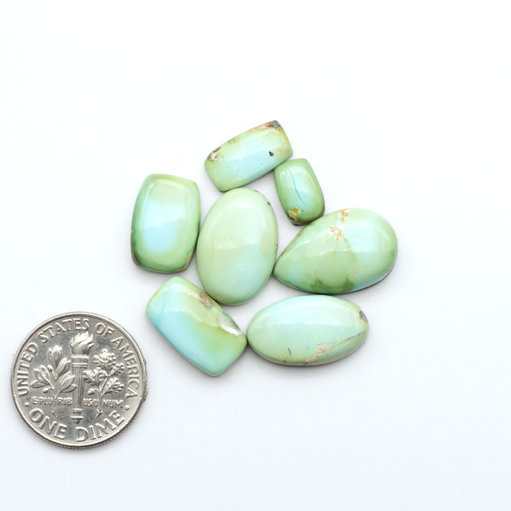 Sonoran Mountain Turquoise cabochons, blue-green color with natural matrix, polished stones on a white background, with a US dime for scale
