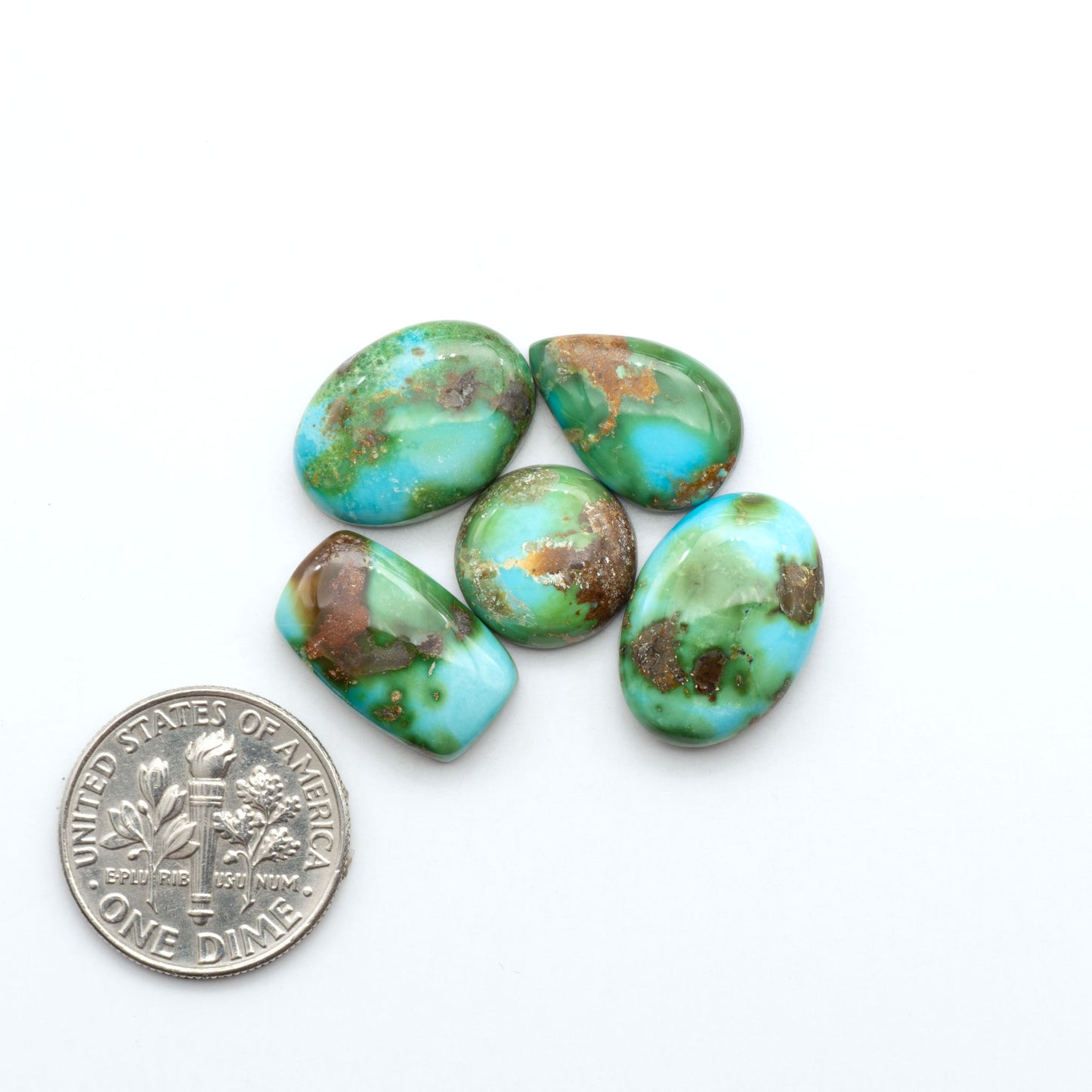 Sonoran Mountain Turquoise cabochons, blue-green color with natural matrix, polished stones on a white background, with a US dime for scale
