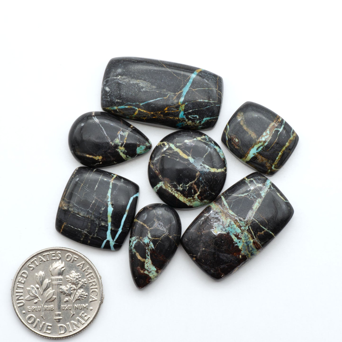Black Jack turquoise cabochons, blue-green color with black matrix, polished stones on a white background with a US dime for scale