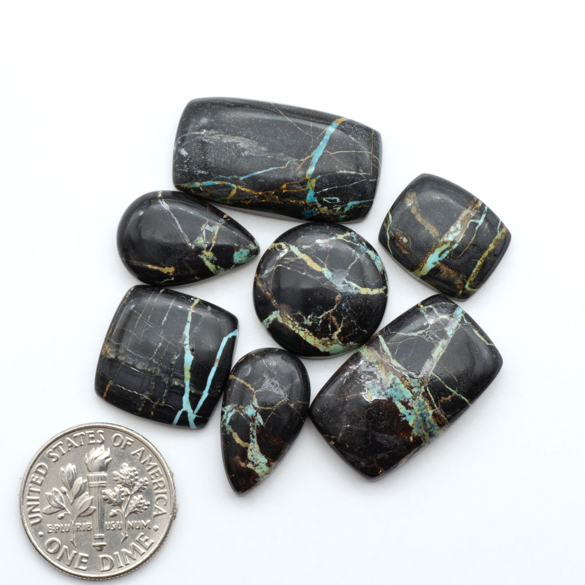 Black Jack turquoise cabochons, blue-green color with black matrix, polished stones on a white background with a US dime for scale