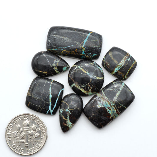 Black Jack turquoise cabochons, blue-green color with black matrix, polished stones on a white background with a US dime for scale