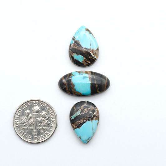 Black Jack turquoise cabochons, blue-green color with black matrix, polished stones on a white background with a US dime for scale