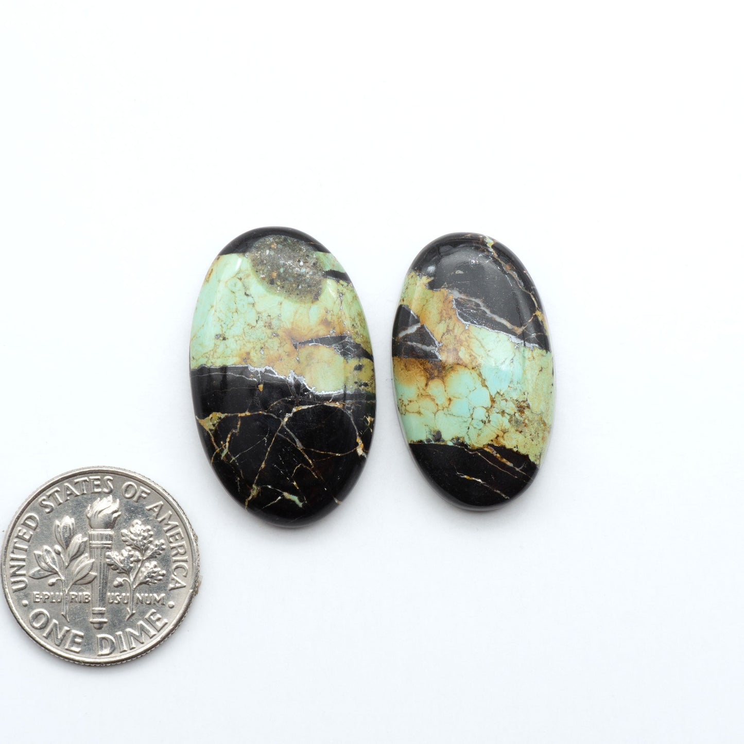 Black Jack turquoise cabochons, blue-green color with black matrix, polished stones on a white background with a US dime for scale