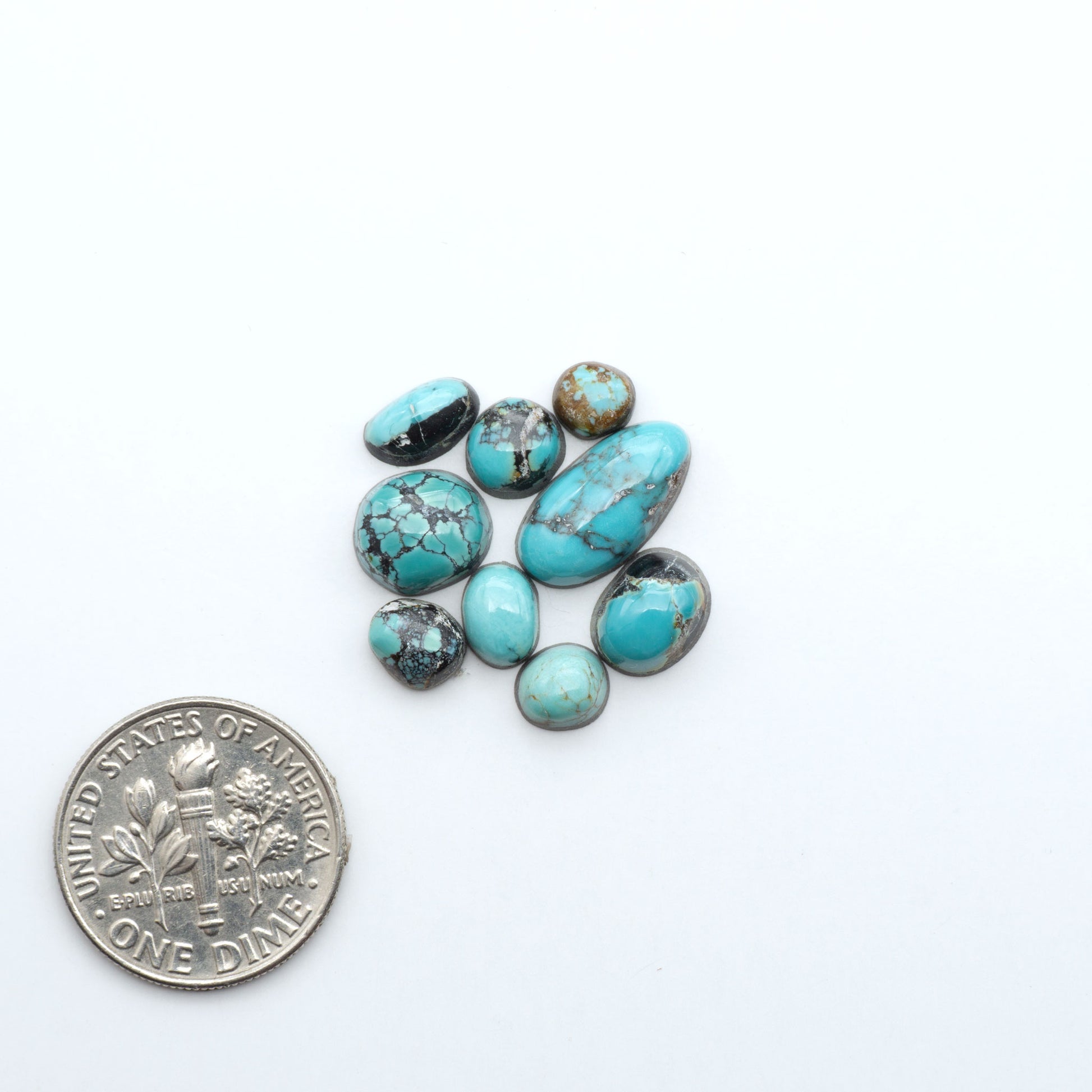 Assorted turquoise cabochon gemstones with varied colors and matrix on a white background with a US dime for scale