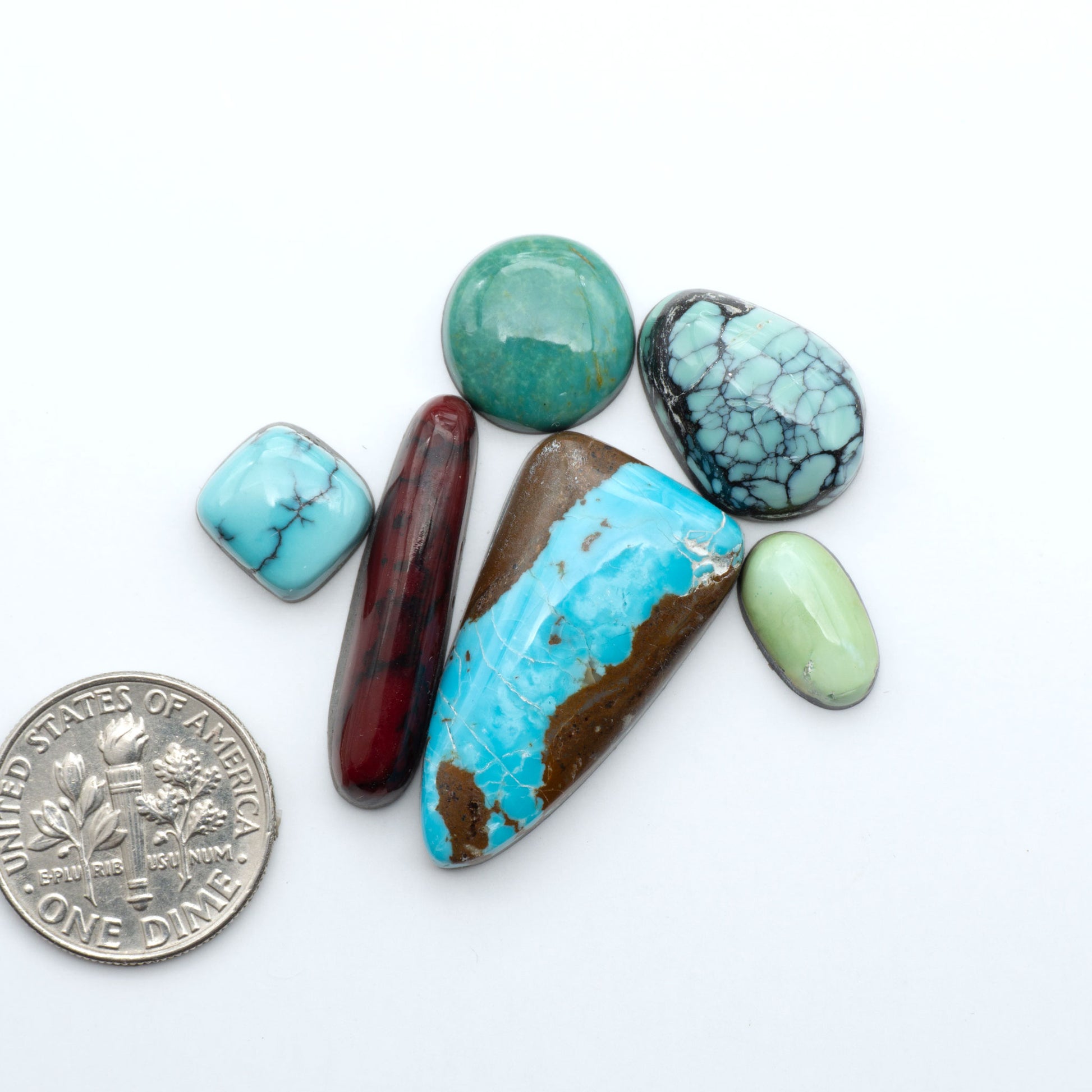 Assorted turquoise cabochon gemstones with varied colors and matrix on a white background with a US dime for scale