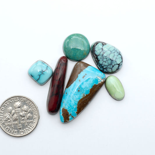 Assorted turquoise cabochon gemstones with varied colors and matrix on a white background with a US dime for scale