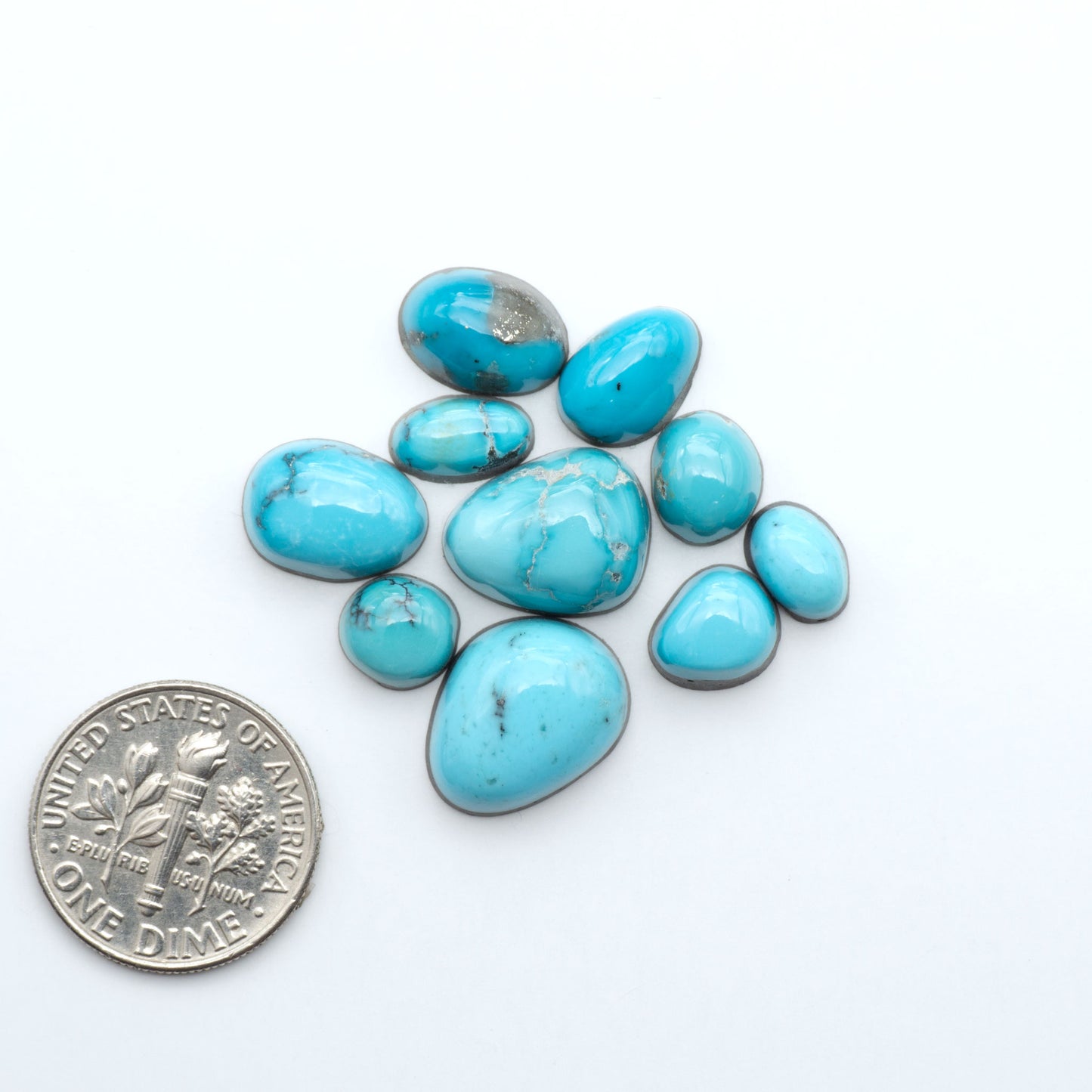 Assorted turquoise cabochon gemstones with varied colors and matrix on a white background with a US dime for scale