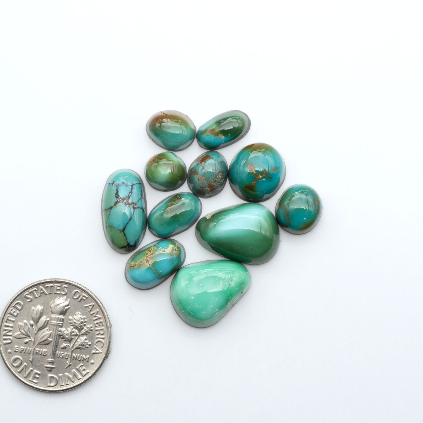 Assorted turquoise cabochon gemstones with varied colors and matrix on a white background with a US dime for scale