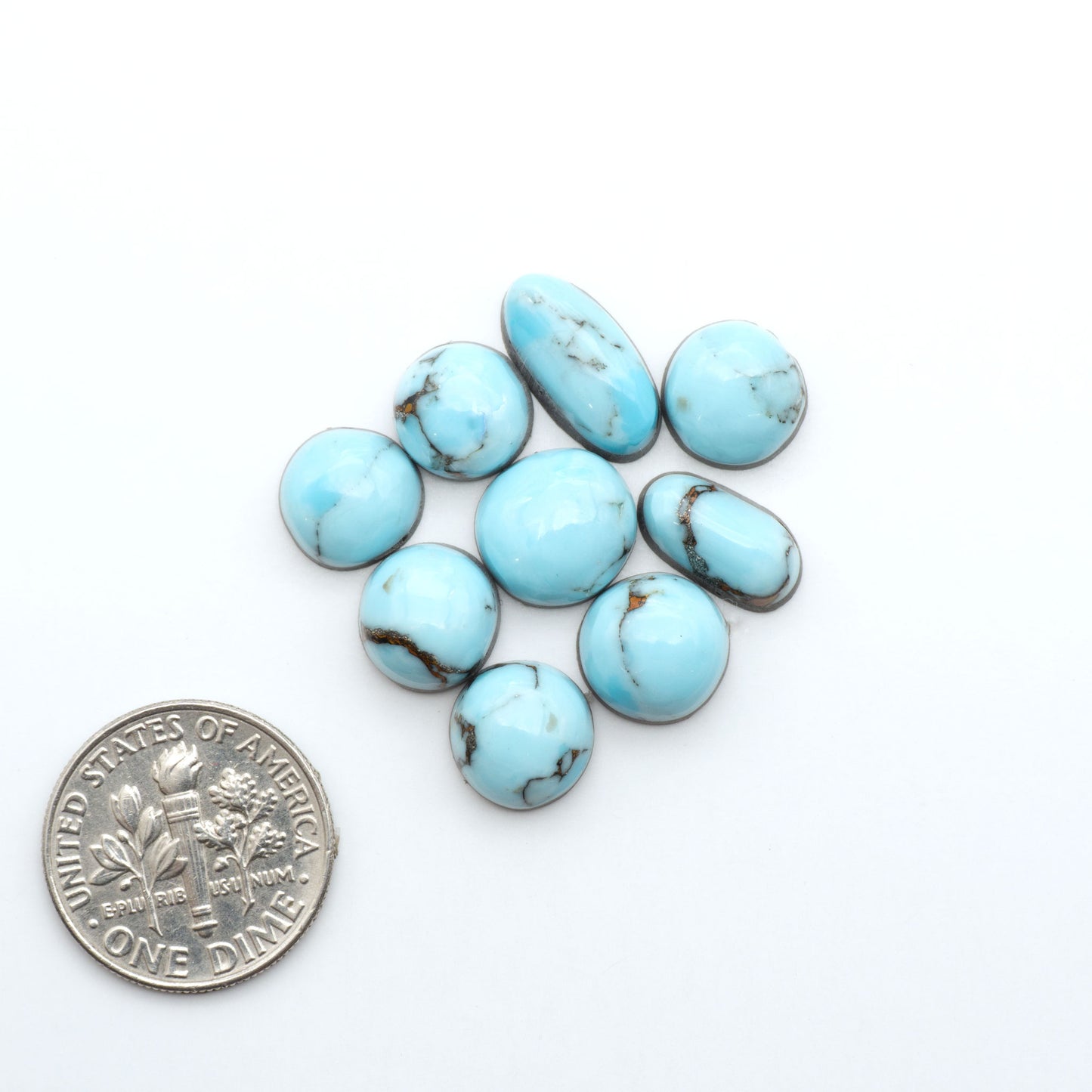 Pressed Turquoise nugget cabochons, composite material with a blue color and dark matrix on a white background, with a US dime for scale.